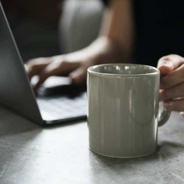 A person sitting at a table with a laptop and a coffee mug, enjoying a beverage while working.