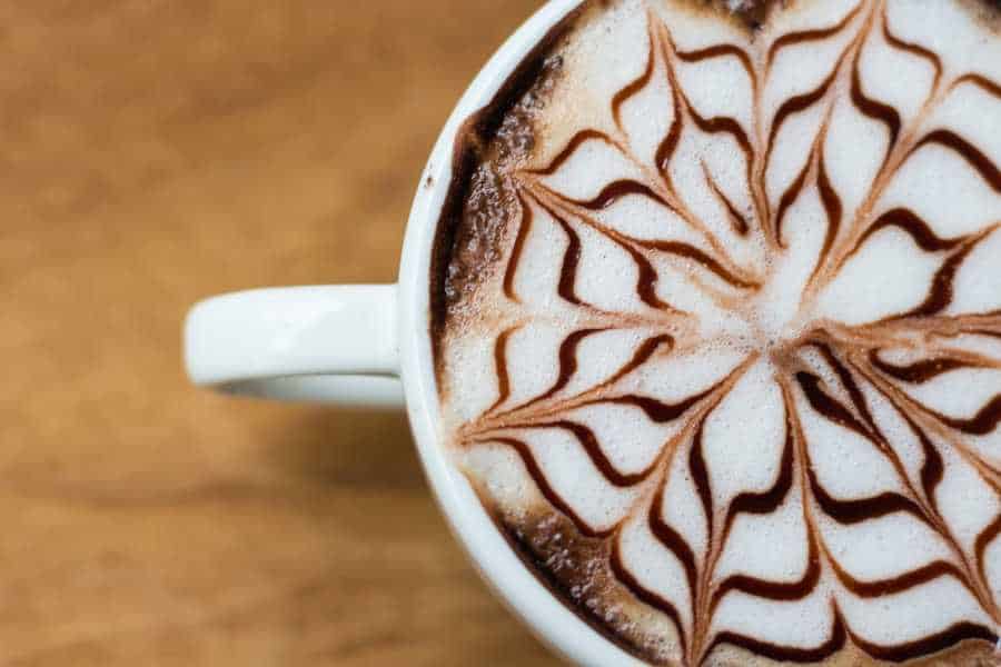 A cappuccino with intricate floral art in the milk foam. Try one at coffee shop in San Marcos