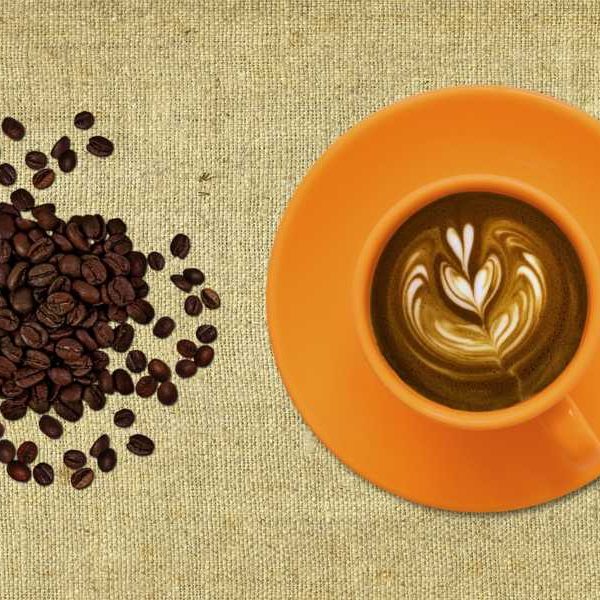 Coffee beans beside latte with heart design in cream in yellow mug