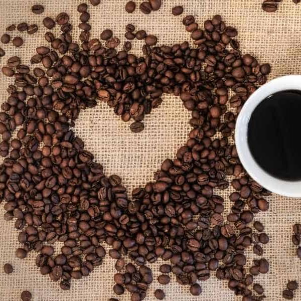 Coffee beans arranged around heart shaped negative space with cup and spoon beside