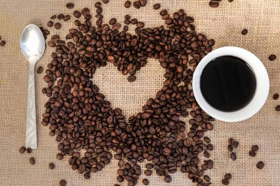 Coffee beans arranged around heart shaped negative space with cup and spoon beside