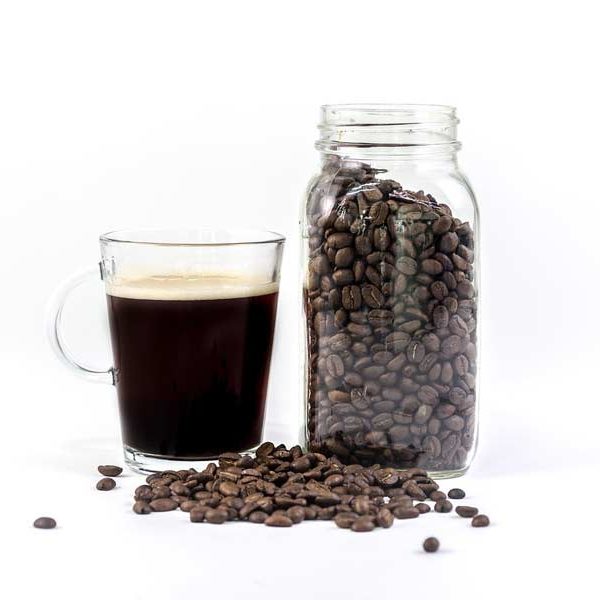 A mason jar of coffee beans next to a glass of freshly brewed coffee