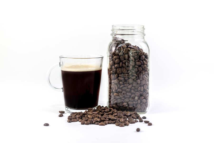 A mason jar of coffee beans next to a glass of freshly brewed coffee