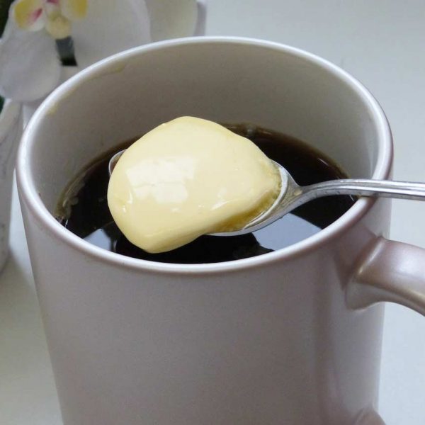 A spoon placing some grass-fed butter into a coffee cup