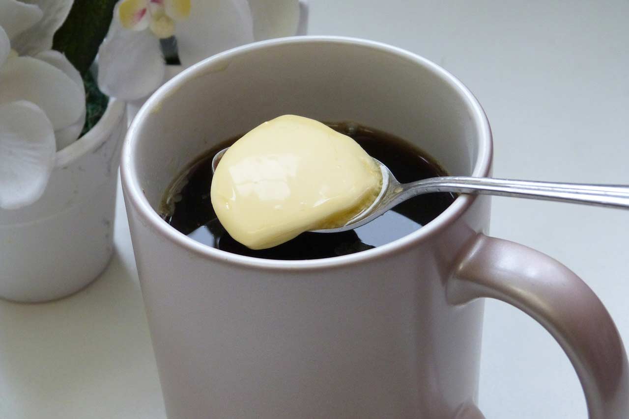 A spoon placing some grass-fed butter into a coffee cup