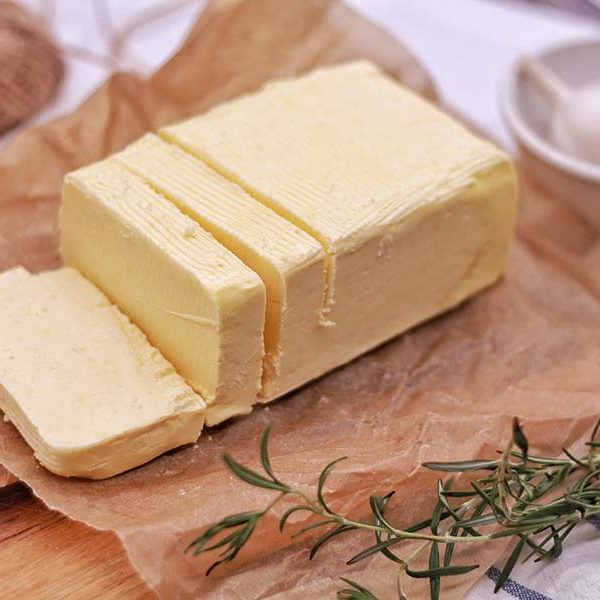 Sliced block of grass-fed butter next to garlic and herbs