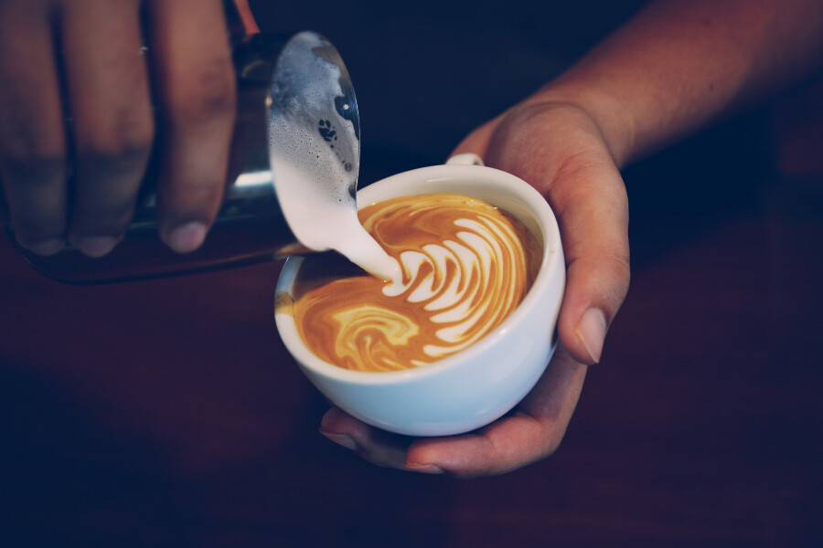 Close up of a barista pouring milk into a latte.