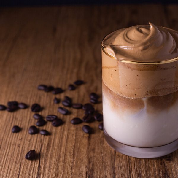 A picture of a Dalgona coffee on a wooden board with coffee beans scattered behind it.