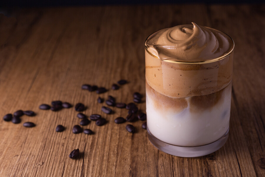 A picture of a Dalgona coffee on a wooden board with coffee beans scattered behind it.