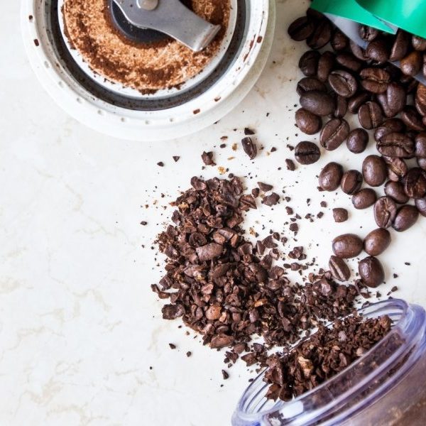 image depicting coffee beans, coffee bean grinder, and spilled whole coffee beans