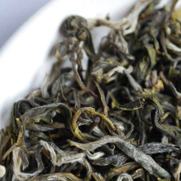 Dried tea leaves in a white bowl on a baby blue surface