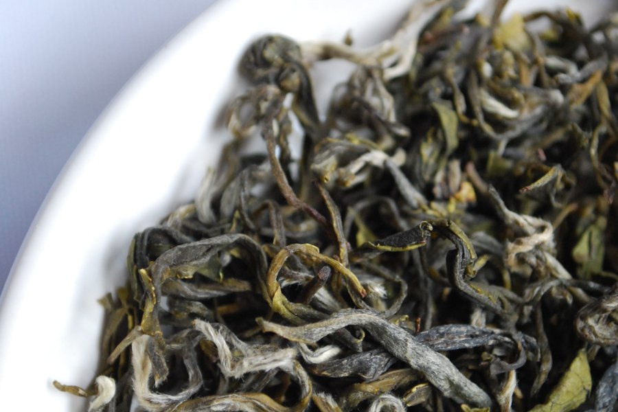 Dried tea leaves in a white bowl on a baby blue surface