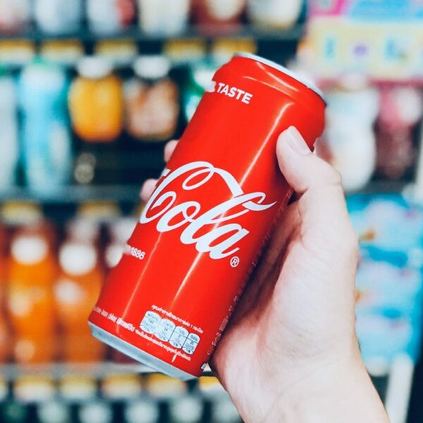 An inviting scene at a coffee shop in San Marcos, TX: A hand holding a refreshing can of Coke amidst a vibrant display of assorted beverages in a cooler.