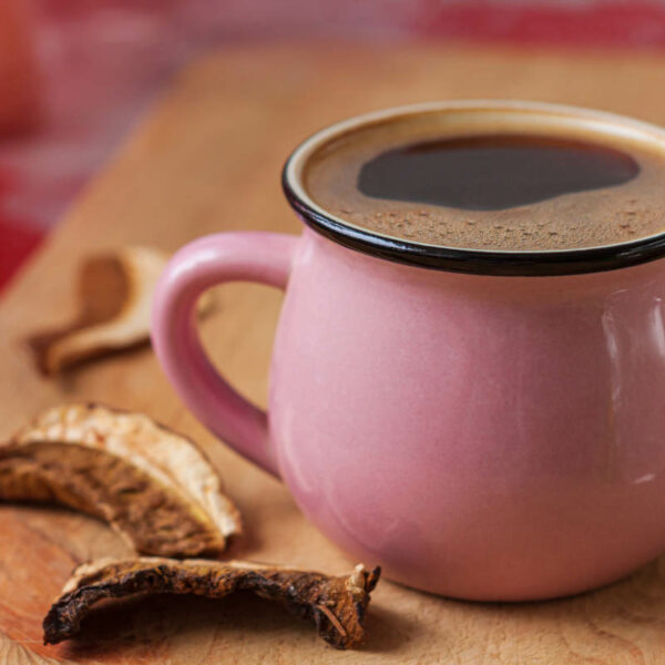 Pink mug filled with a dark coffee-like beverage placed next to slices of dried mushrooms