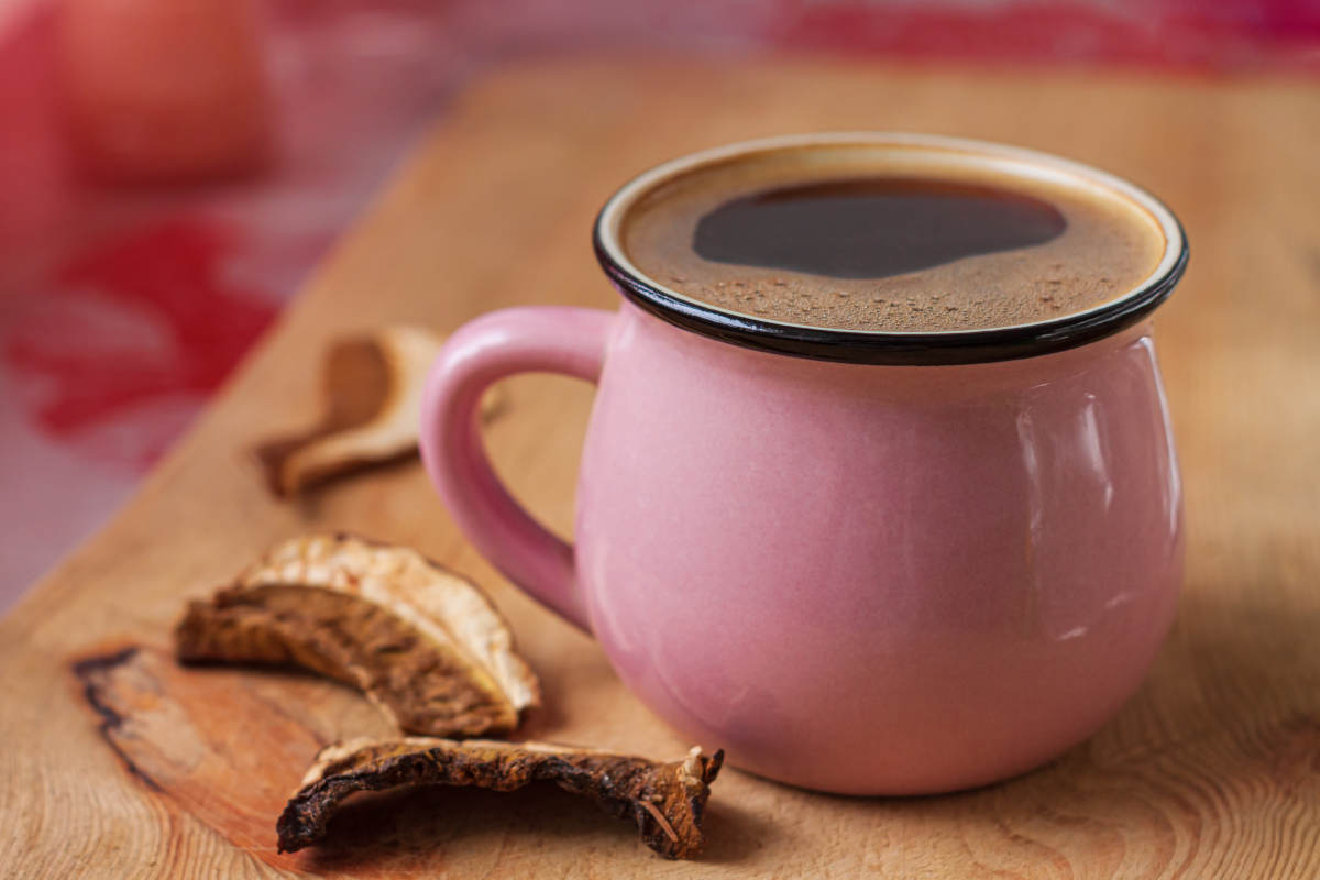 Pink mug filled with a dark coffee-like beverage placed next to slices of dried mushrooms