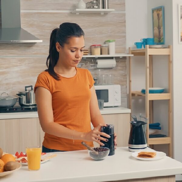 A woman in an orange shirt joyfully prepares breakfast in the kitchen, showcasing Fun-and-Creative-Uses-for-Coffee-Grounds-at-Home.