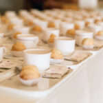 Rows of prepared trays with coffee cups and croissants line a counter at an event.