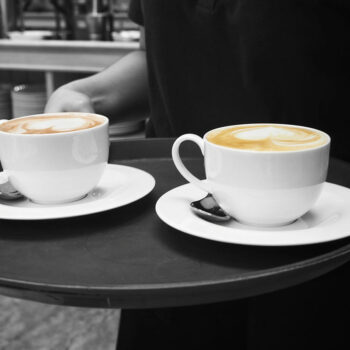 A barista is holding a tray with two lattes.