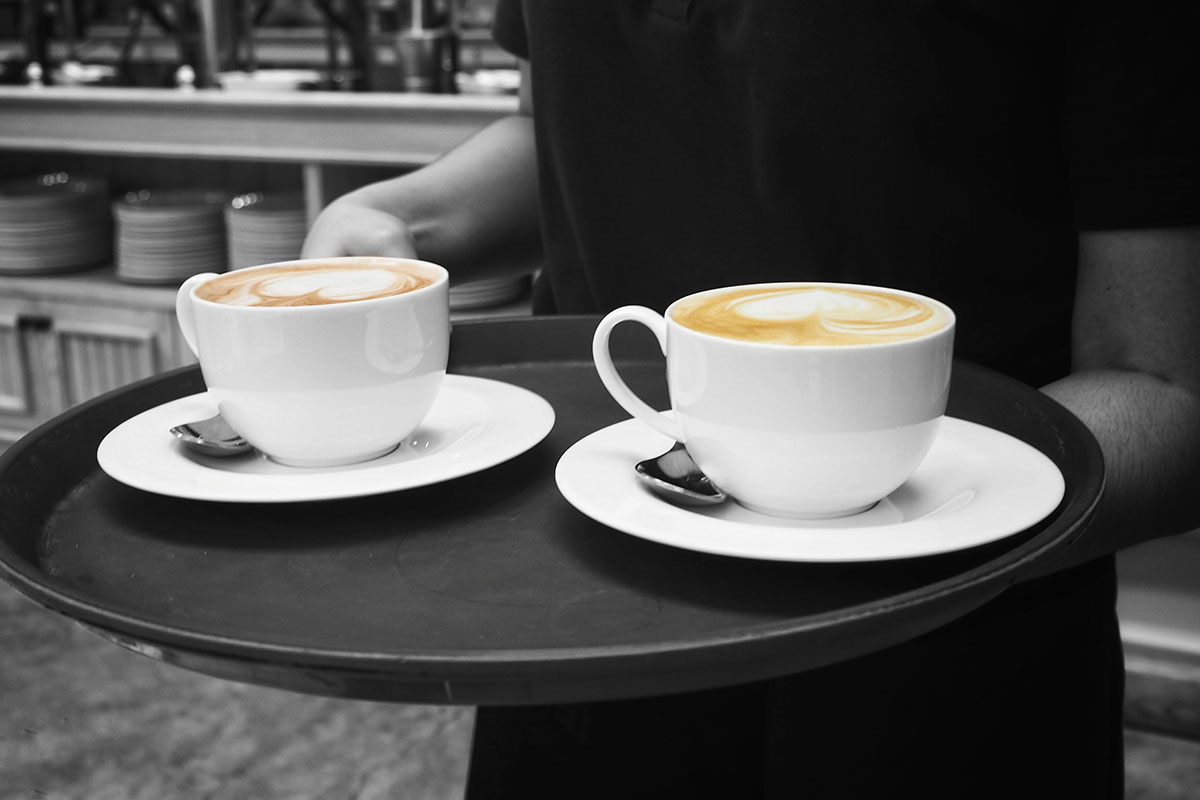 A barista is holding a tray with two lattes.
