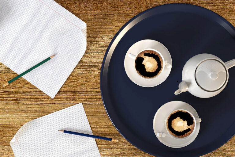 A wooden table with a dark round tray featuring two white cups of coffee and a teapot, accompanied by two sheets of graph paper and colored pencils.