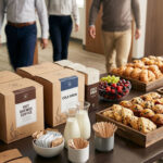 An insulated coffee dispenser with a "CRAFT COFFEE" label and a large tray of assorted pastries, including croissants and mini muffins, are arranged on a wooden catering table in a bright, modern conference room, ready to serve attendees who can be seen gathering in the blurred background.