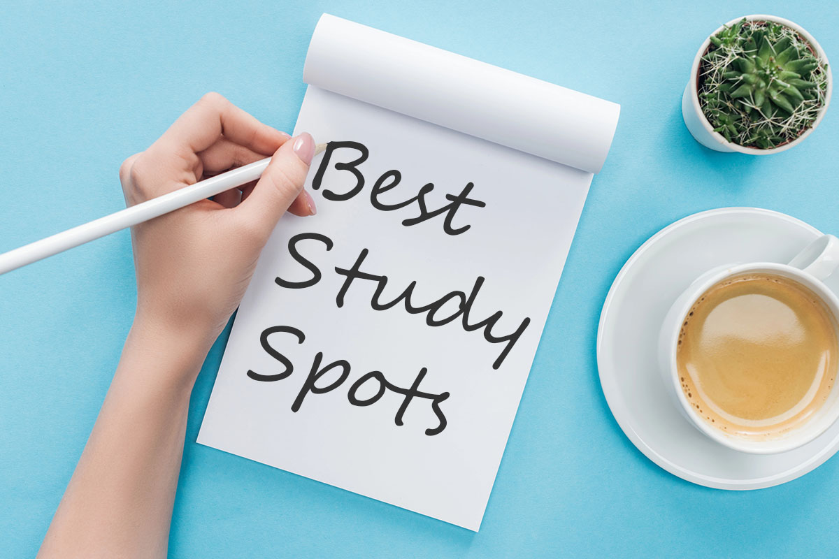 A top-down view of a hand writing "Best Study Spots" on a white notepad, positioned on a light blue desk next to a coffee cup and a small cactus.